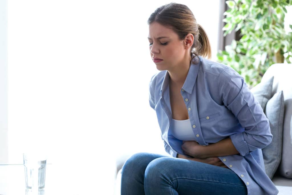 Shot of unhealthy young woman with stomachache leaning on the couch at home.